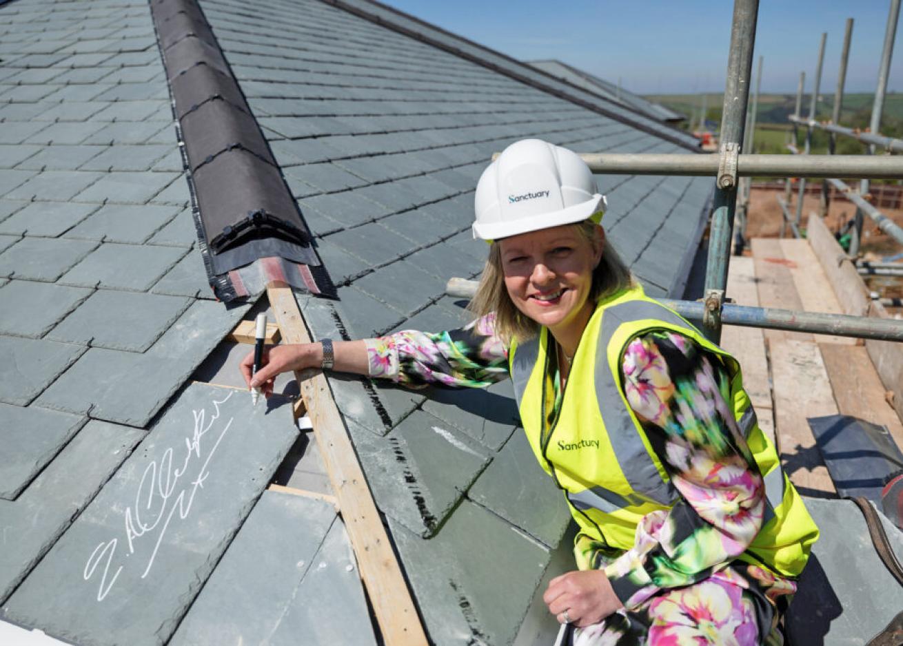 A woman wearing a hard hat and a high-visibility vest is working on a roof covered with slate tiles.