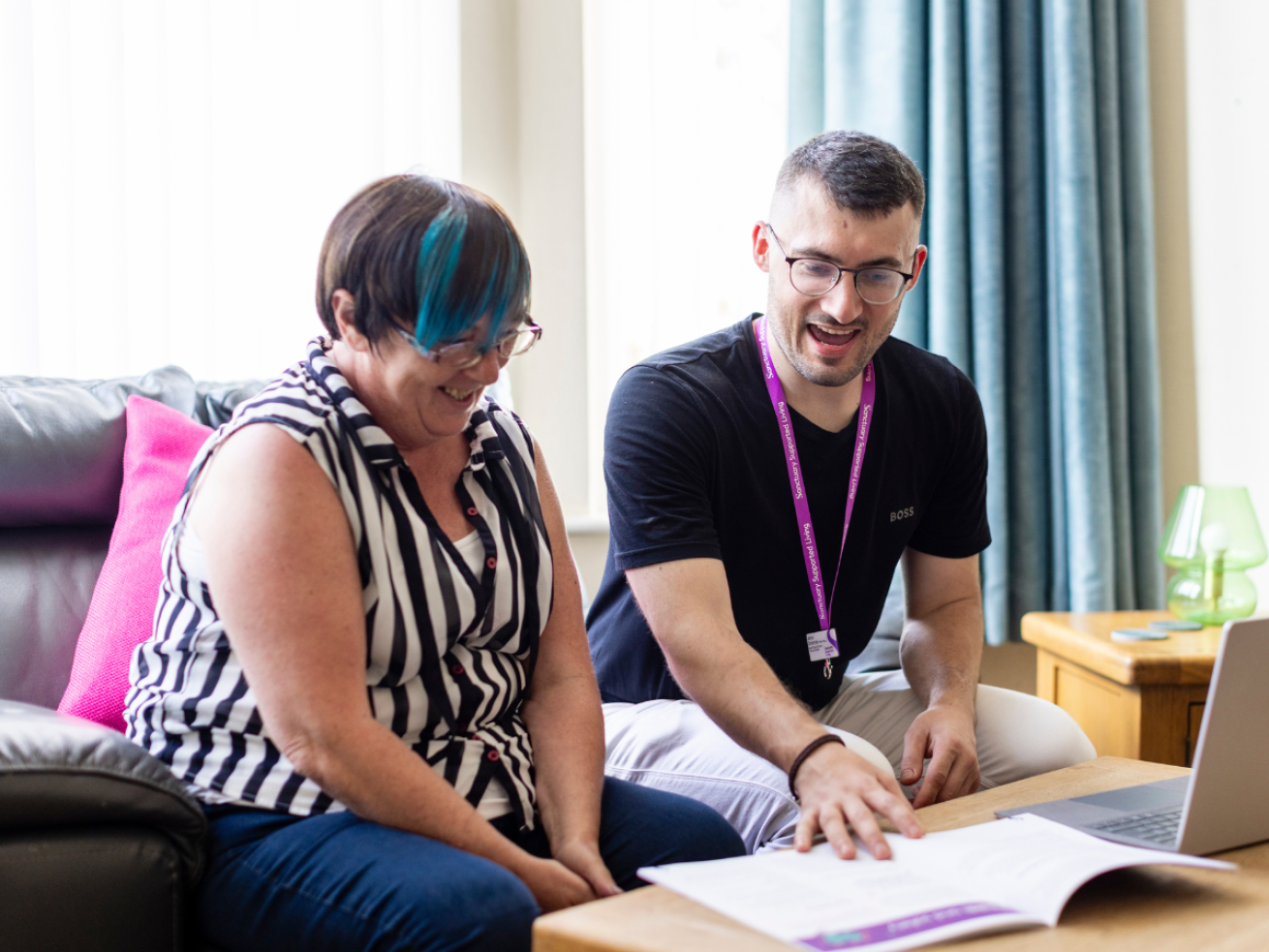 A man wearing a lanyard points at a booklet while sat next to a woman