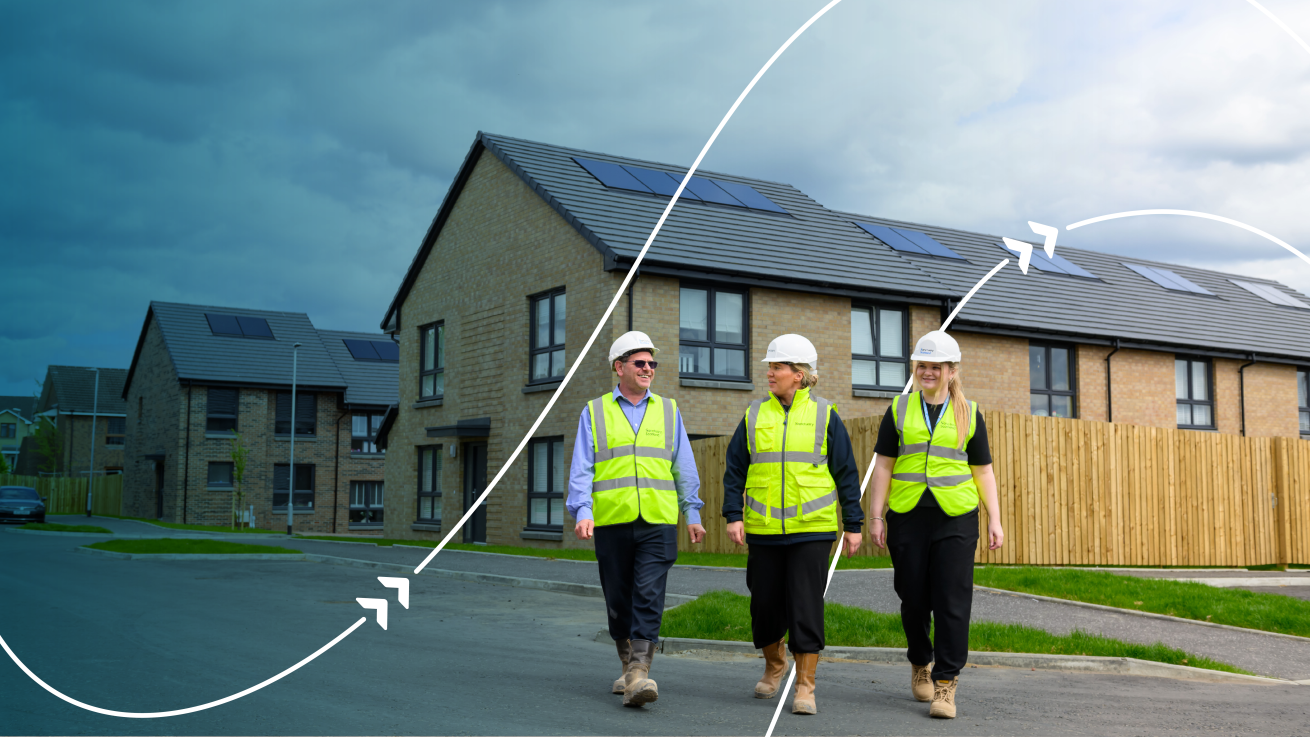 Three people wearing high-visibility clothing and hard hats walking through a residential housing development with solar panels on the roofs.