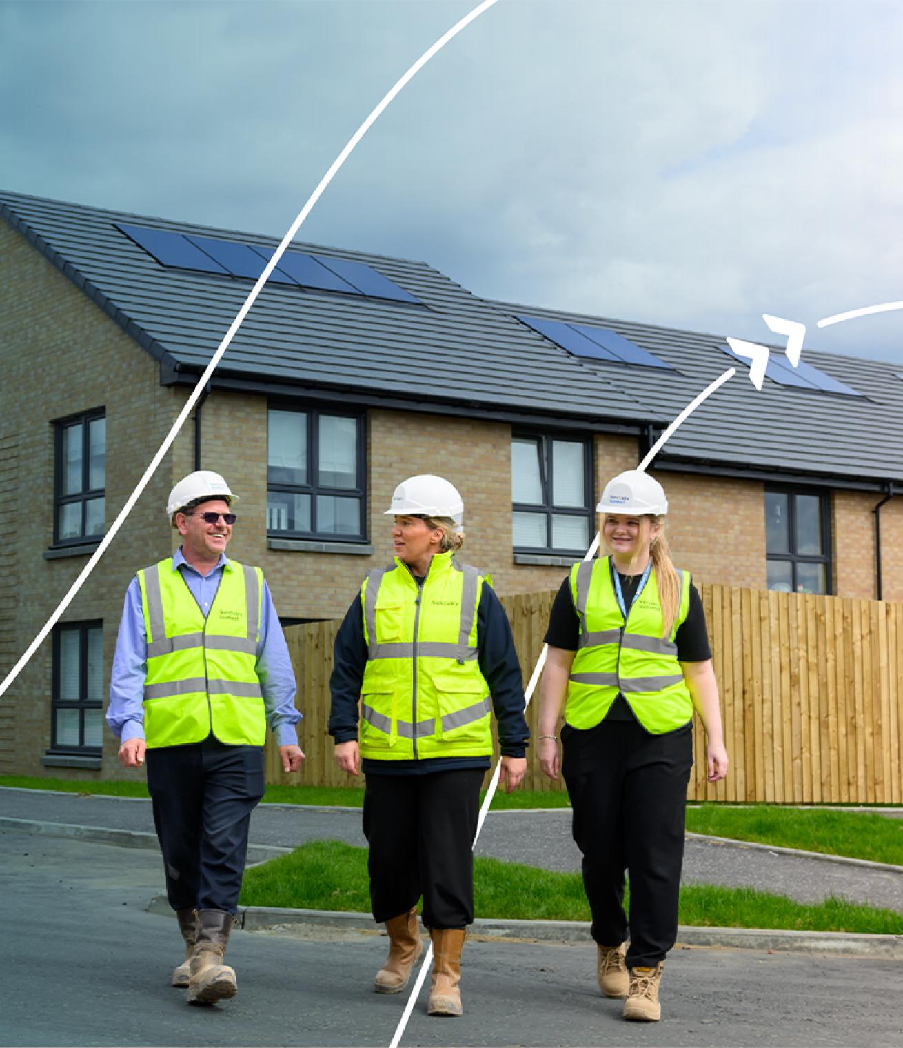 Three people wearing high-visibility clothing and hard hats walking through a residential housing development with solar panels on the roofs.