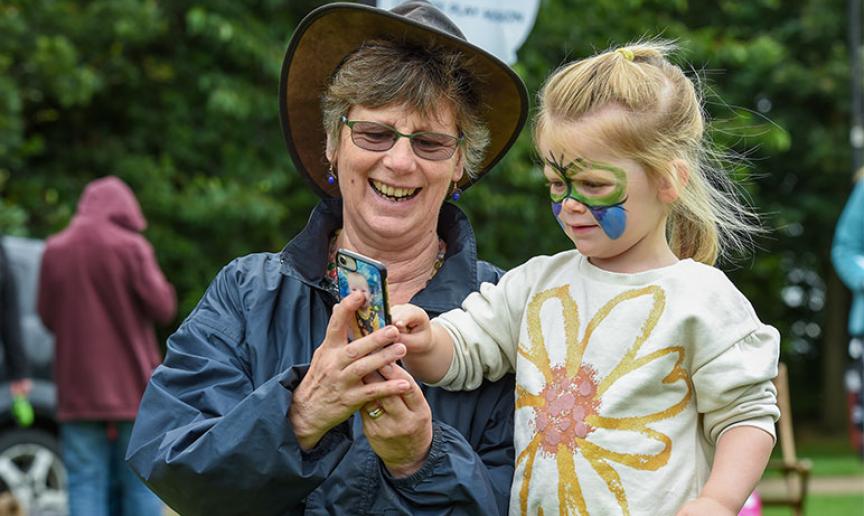A woman showing her grandchild something on her phone during a community event. A woman showing her grandchild something on her phone during a community event.