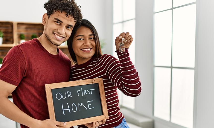 Two people holding a chalkboard saying our first home and holding keys