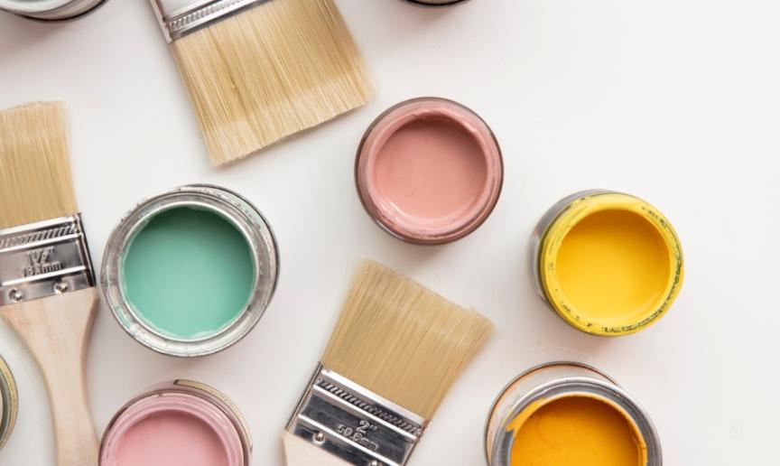 A collection of open paint pots of bright colours with several paintbrushes