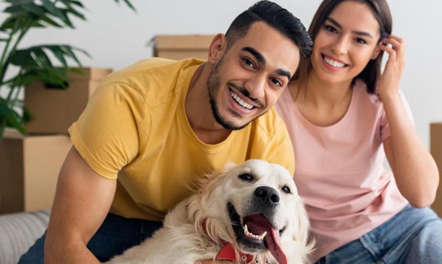 Two people sat with a dog in front of moving boxes 