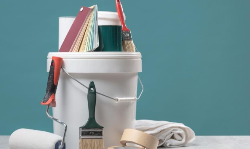 A tub of paint and paintbrushes against a newly painted blue wall