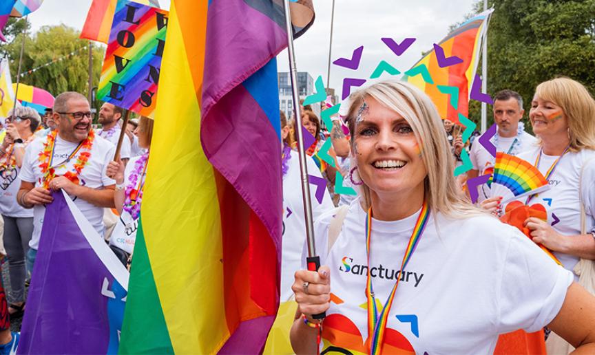 Sanctuary inclusion for all Sanctuary staff and residents wearing white shirts with rainbow hearts on carrying rainbow flags taking part in a march for a PRIDE event