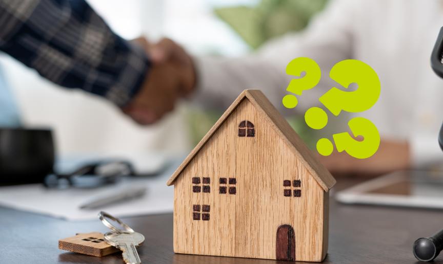 A wooden model of a house on a table next to a keychain with a silver key and a model house keyring on it. There are question marks around the model house and a handshake in the background