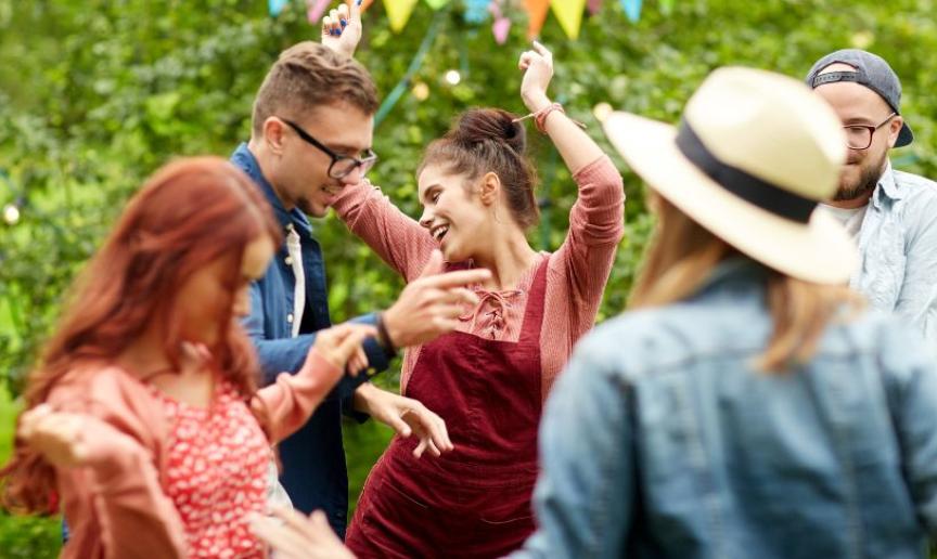 A group of men and women dancing in a garden decorated with multicoloured bunting.
