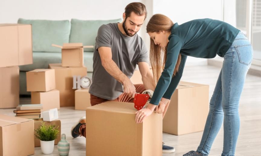A couple in a room full of boxes taping them up preparing to move house