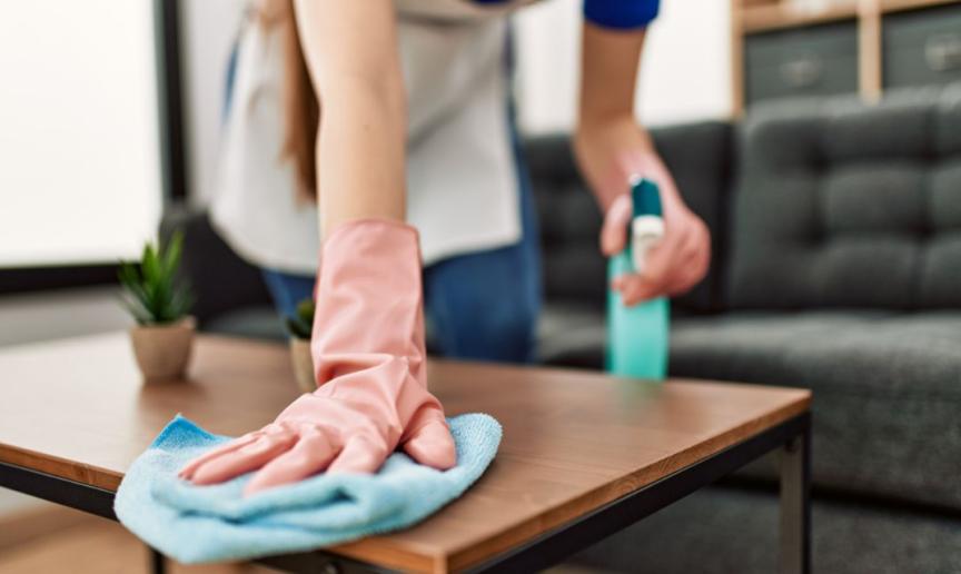 A person wearing rubber gloves and a cleaning spray bottle wiping down a coffee table