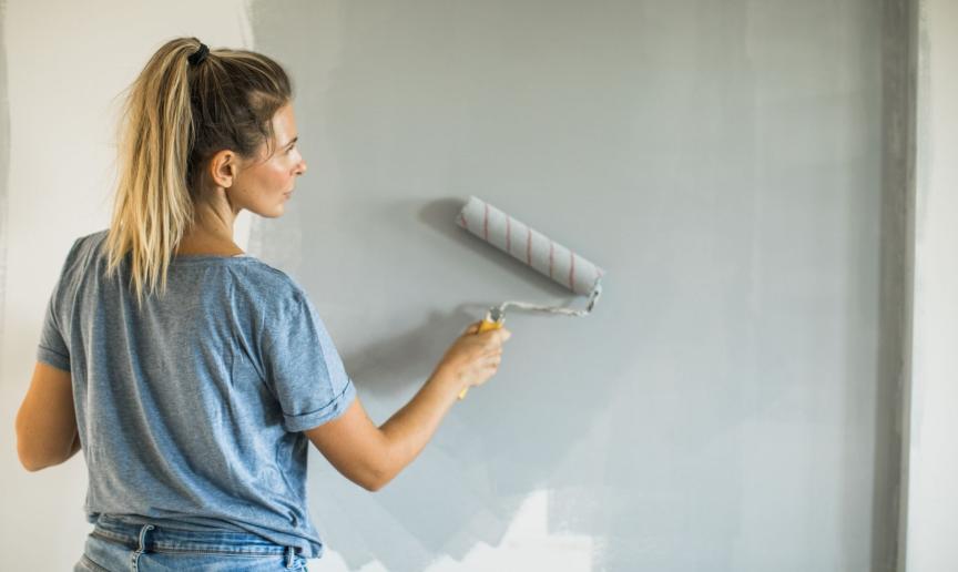 A woman with blonde hair is painting a wall with a paint roller.