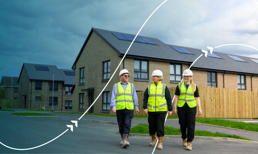 Three people wearing high-visibility clothing and hard hats walking through a residential housing development with solar panels on the roofs.