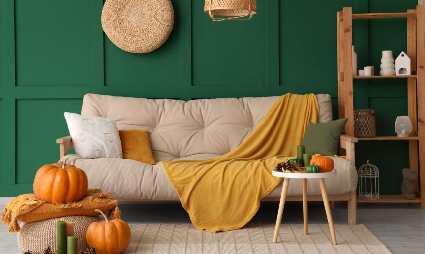 Cosy autumn living room with a cream sofa, mustard throw, pumpkins and a dark green feature wall.