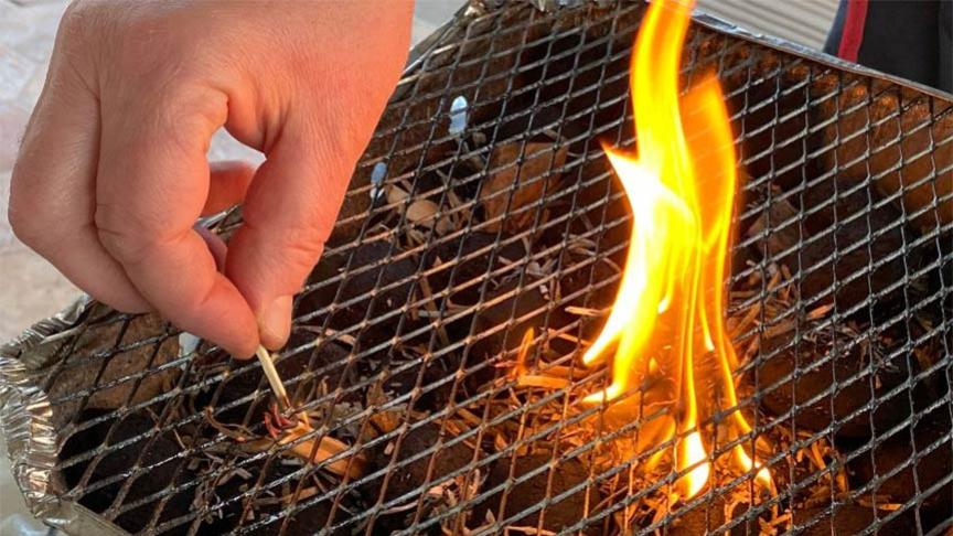 A hand lighting a disposable barbecue with a match