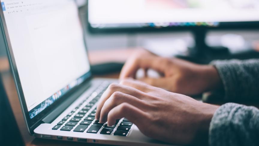 Hands typing on a laptop with a second monitor in the background