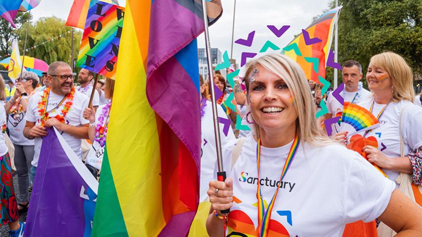Sanctuary inclusion for all Sanctuary staff and residents wearing white shirts with rainbow hearts on carrying rainbow flags taking part in a march for a PRIDE event