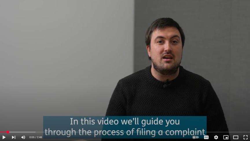 A man talks to the camera, captions read 'In this video we'll guide you through the process of filing a complaint'