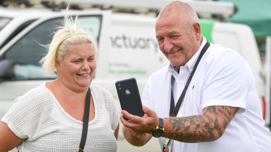 Two people chatting near a white van—one shows something on their phone. The van says “A better life, no conditions.”