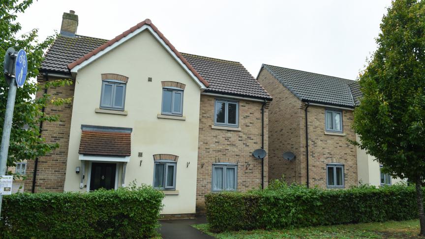 Two modern semi‑detached houses with cream and brick walls, grey windows, hedges and a footpath in front.