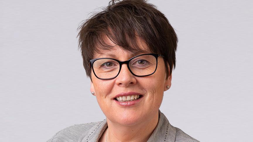 Head-and-shoulders portrait of Kathryn Fox-Rogers wearing glasses and a light grey jacket against a grey background.