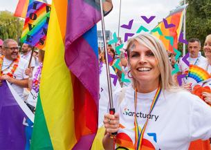 Sanctuary staff and residents wearing white shirts with rainbow hearts on carrying rainbow flags taking part in a march for a PRIDE event