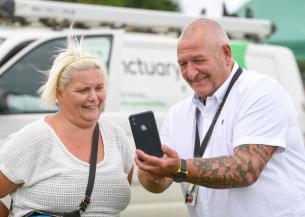 Two people chatting near a white van—one shows something on their phone. The van says “A better life, no conditions.”