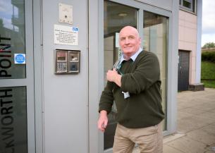 Person wearing a green sweater and beige trousers exiting a building labeled 'Rockworth Point'