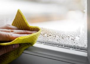 Hand wiping condensation from a window, showing early signs of damp.