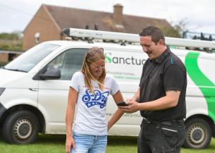 Two people stand outside on a windy day in front of a Sanctuary maintenance van. Sanctuary repairs staff member is showing a resident something on his phone, they are both smiling.