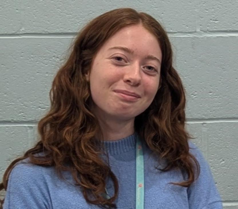 Headshot photo of woman with long hair, wearing a Sanctuary lanyard and smiling at the camera
