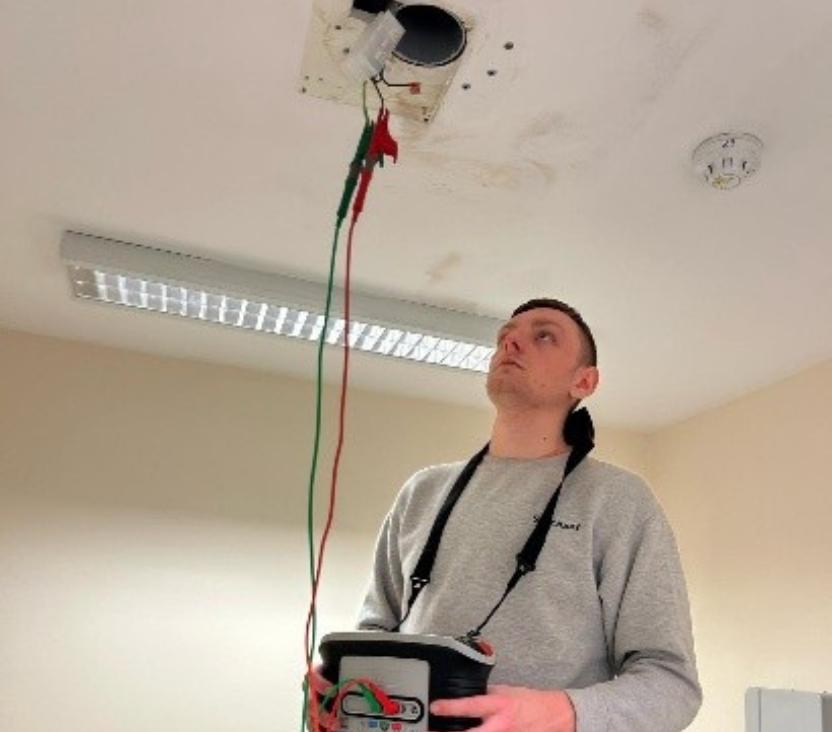 Image shows a man looking at the ceiling or a building and performing a safety test for some equipment