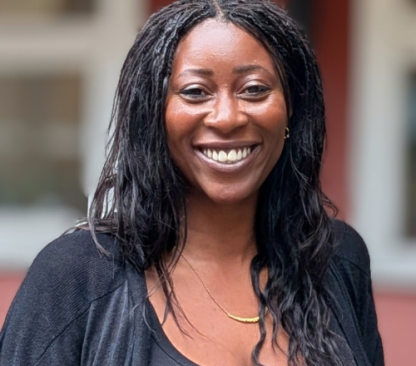 A smiling woman with long dark hair stands in front of a block of flats