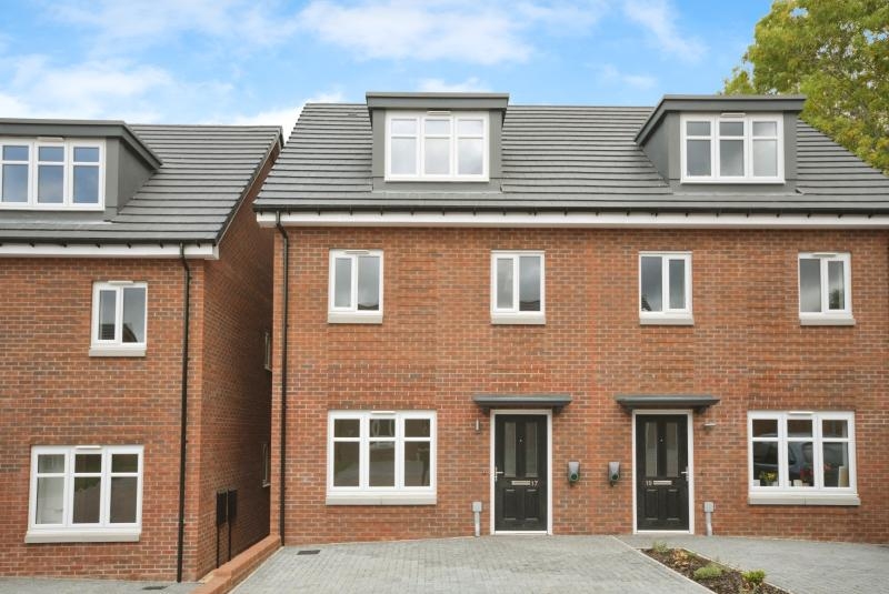 Front view of a red brick semi-detached house with white windows and a black front door.